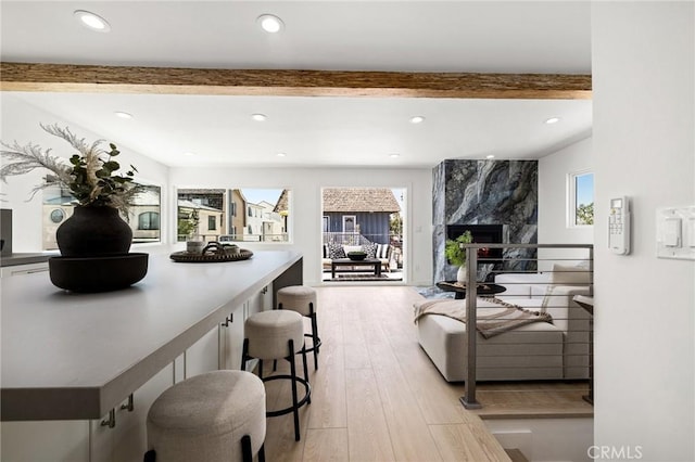 living room featuring beamed ceiling, a wealth of natural light, a fireplace, and light wood-type flooring