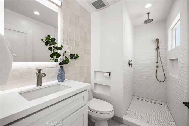 bathroom with tiled shower, vanity, and toilet