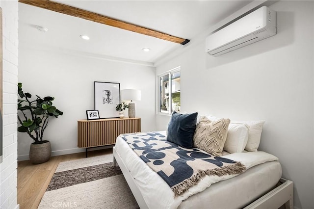 bedroom featuring a wall mounted air conditioner, beam ceiling, and light hardwood / wood-style flooring