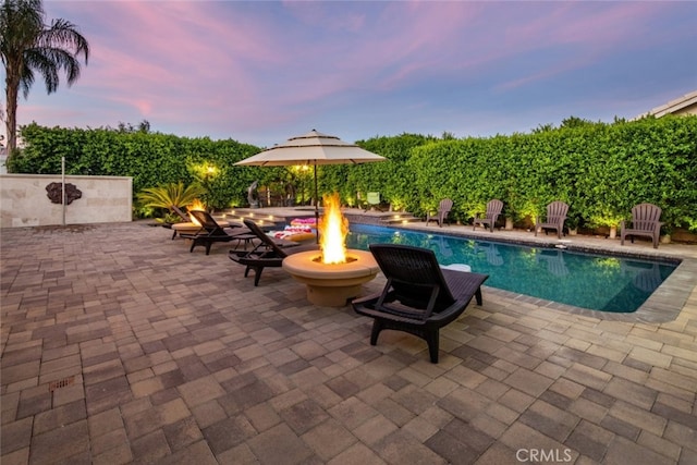 pool at dusk with a fire pit and a patio area