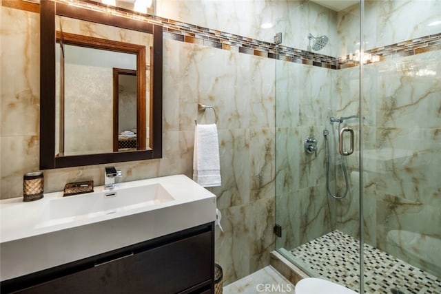 bathroom with tile walls, a shower with door, vanity, and toilet