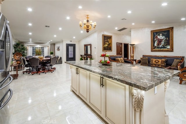 kitchen featuring a center island, a breakfast bar area, an inviting chandelier, dark stone countertops, and cream cabinets