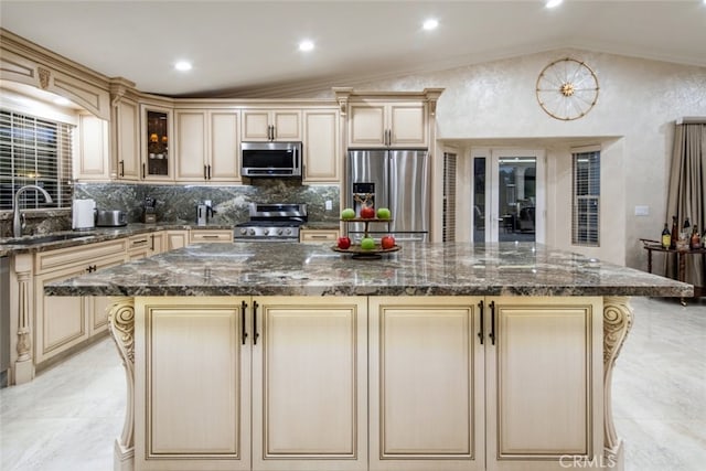 kitchen with appliances with stainless steel finishes, dark stone countertops, vaulted ceiling, a kitchen island, and sink