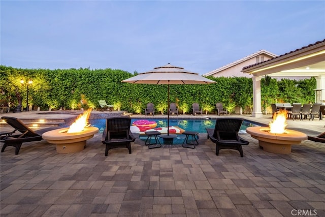 patio terrace at dusk with a fenced in pool and a fire pit