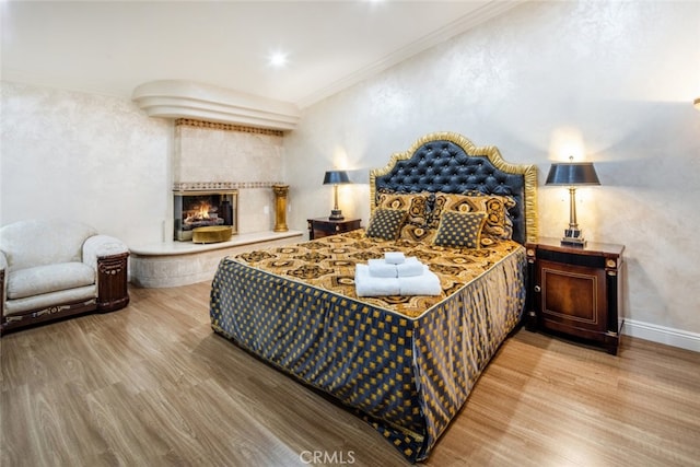 bedroom with wood-type flooring, crown molding, and a tile fireplace