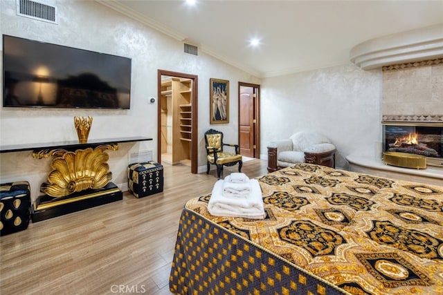 bedroom with ornamental molding, lofted ceiling, a tile fireplace, and light hardwood / wood-style flooring