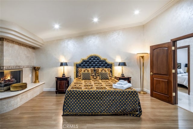 bedroom with light wood-type flooring, a fireplace, and crown molding