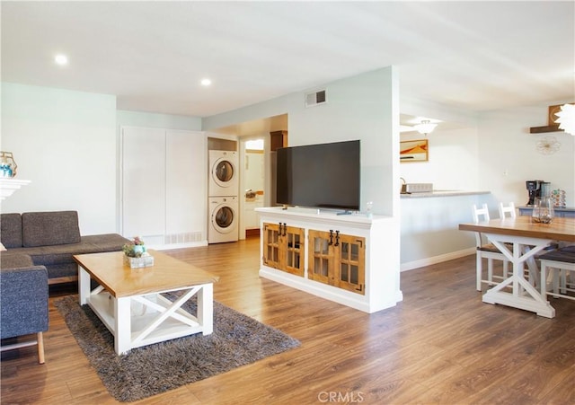 living room with stacked washer / drying machine, wood finished floors, baseboards, and recessed lighting