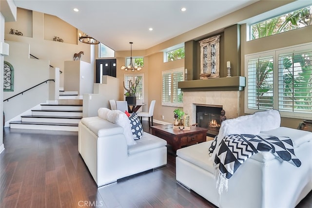 living room featuring a tiled fireplace, dark hardwood / wood-style floors, high vaulted ceiling, and a notable chandelier