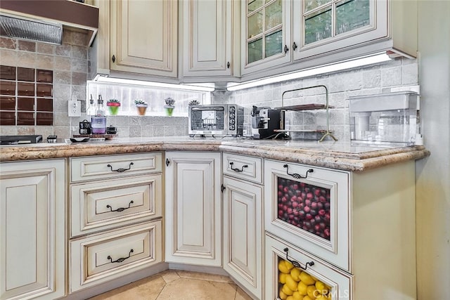 kitchen with light stone countertops, backsplash, cream cabinets, and light tile patterned floors