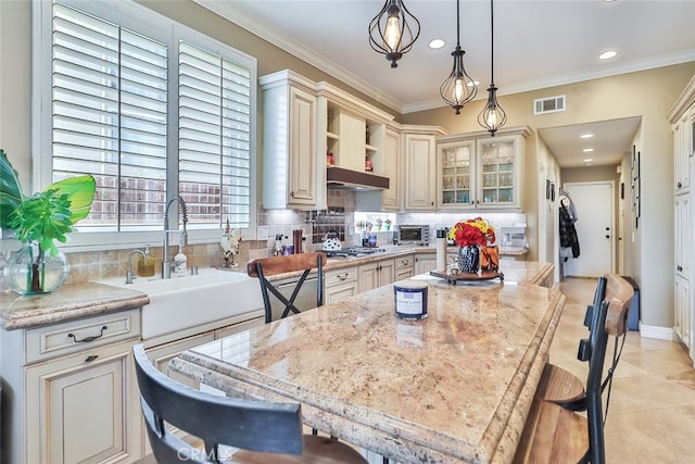 kitchen featuring tasteful backsplash, decorative light fixtures, a center island, light stone countertops, and crown molding