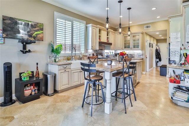 kitchen featuring hanging light fixtures, light stone countertops, a center island, cream cabinets, and sink