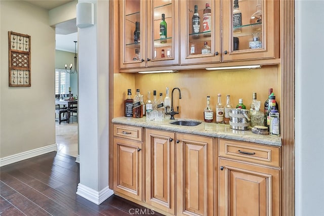 bar with light stone countertops, dark wood-type flooring, a chandelier, and sink