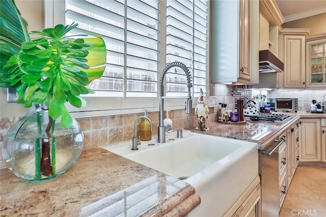 kitchen featuring cream cabinetry, decorative backsplash, light stone counters, ornamental molding, and sink