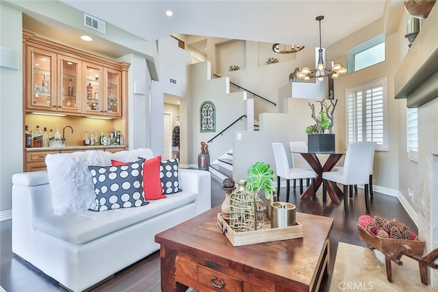 living room featuring an inviting chandelier, a high ceiling, bar area, and dark hardwood / wood-style flooring