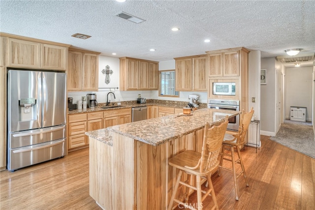 kitchen featuring appliances with stainless steel finishes, light stone countertops, a kitchen bar, light hardwood / wood-style flooring, and sink