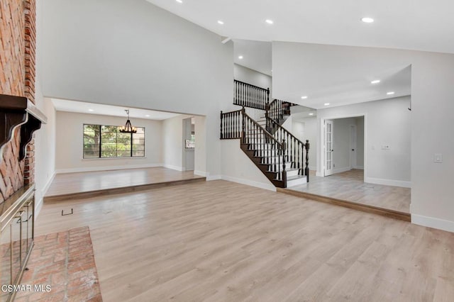 unfurnished living room with high vaulted ceiling, light hardwood / wood-style flooring, a brick fireplace, and a notable chandelier