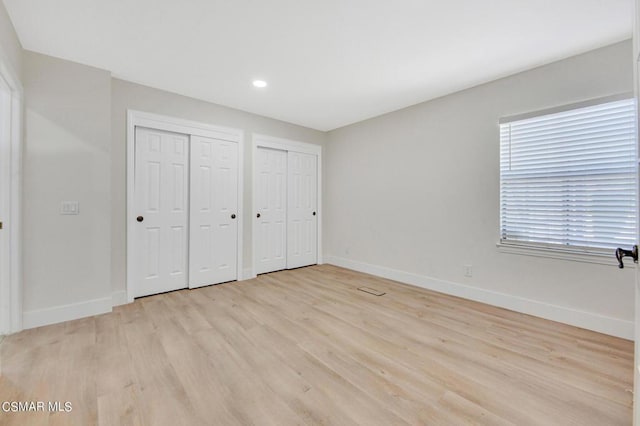 unfurnished bedroom featuring light hardwood / wood-style floors and multiple closets