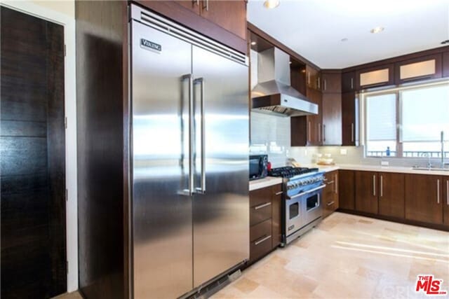 kitchen with backsplash, dark brown cabinetry, sink, wall chimney range hood, and high quality appliances