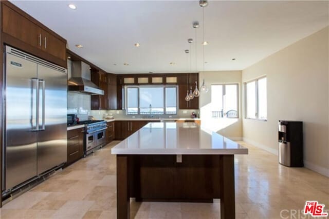 kitchen featuring wall chimney exhaust hood, hanging light fixtures, high quality appliances, dark brown cabinets, and a kitchen island