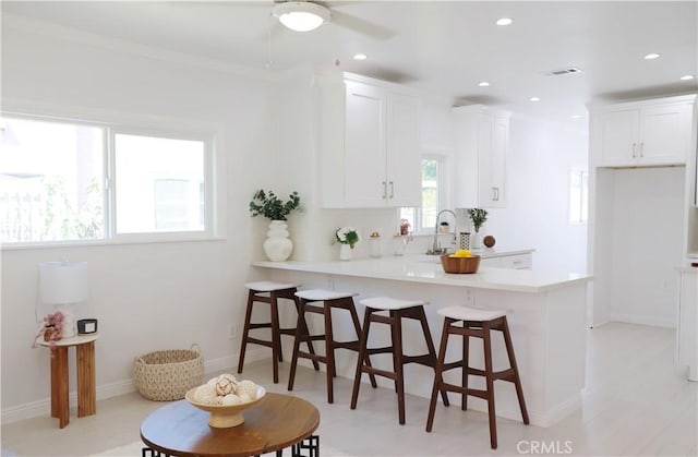 kitchen with kitchen peninsula, a kitchen bar, ceiling fan, sink, and white cabinetry