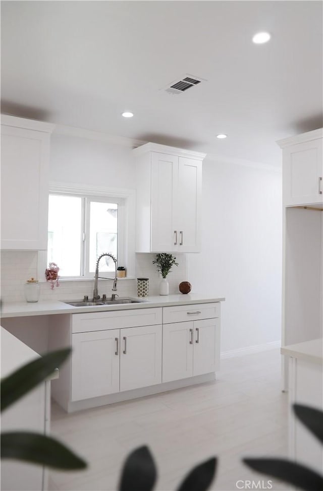 kitchen with decorative backsplash, sink, white cabinets, and crown molding