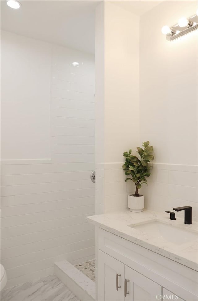 bathroom featuring tiled shower, vanity, and tile walls