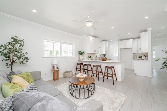 living room featuring ceiling fan, light wood-type flooring, ornamental molding, and sink