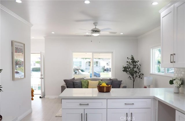 kitchen with white cabinets, light hardwood / wood-style flooring, ceiling fan, ornamental molding, and kitchen peninsula