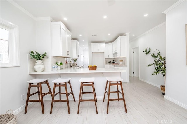 kitchen with kitchen peninsula, white cabinets, tasteful backsplash, and a breakfast bar area