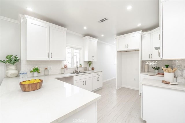 kitchen with backsplash, white cabinets, sink, light hardwood / wood-style flooring, and ornamental molding