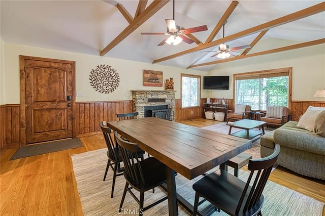 dining space featuring vaulted ceiling with beams, ceiling fan, a stone fireplace, and light wood-type flooring