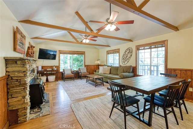 dining area featuring light wood-type flooring, vaulted ceiling with beams, a wood stove, and ceiling fan