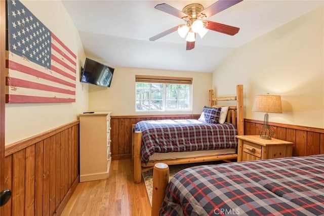 bedroom featuring ceiling fan, light wood-type flooring, wooden walls, and vaulted ceiling