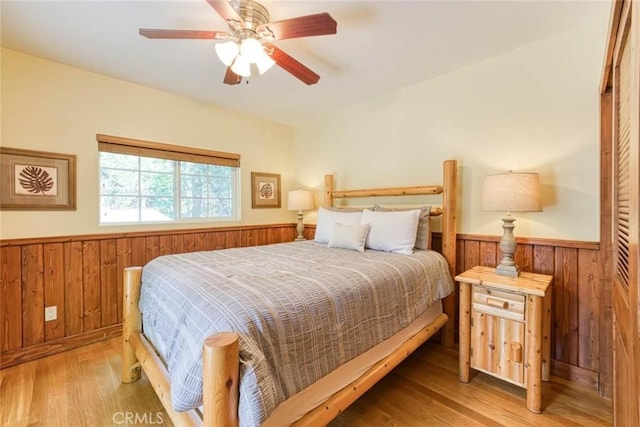 bedroom with light wood-type flooring, ceiling fan, and wooden walls