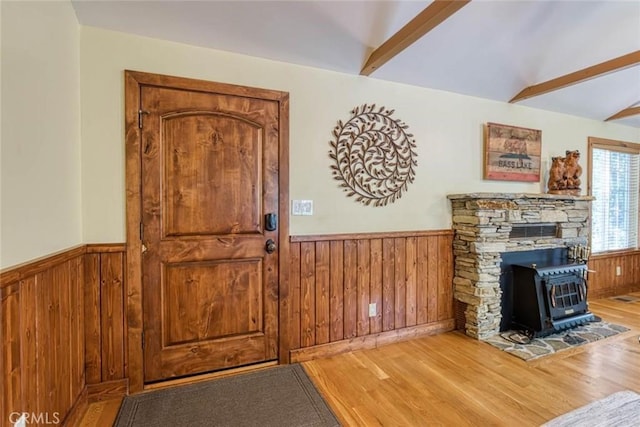 foyer with wood-type flooring, vaulted ceiling with beams, and a wood stove