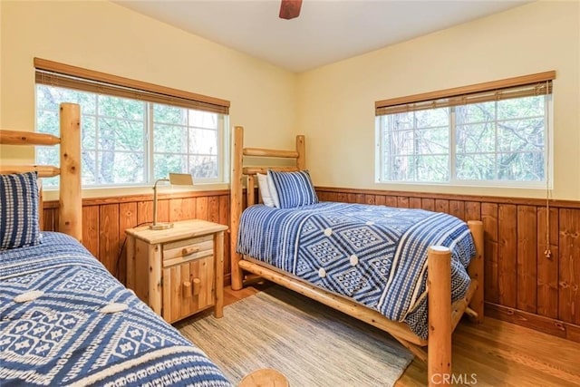 bedroom with light hardwood / wood-style floors, ceiling fan, and wooden walls