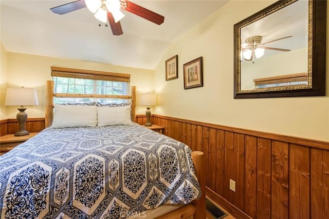 bedroom with vaulted ceiling, ceiling fan, and wooden walls