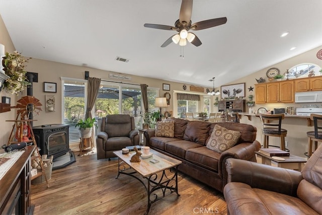 living room with vaulted ceiling, ceiling fan, a wood stove, and a wealth of natural light