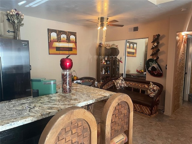 bar featuring light stone countertops, black fridge, and ceiling fan