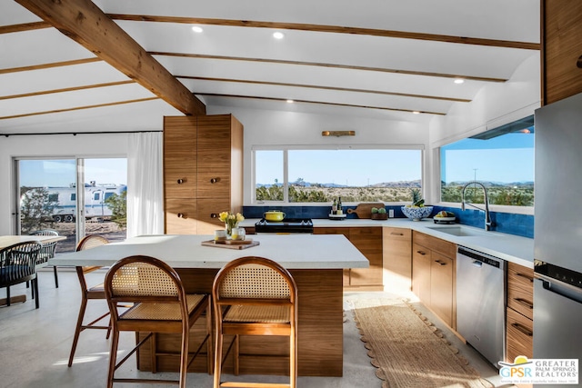 kitchen with a breakfast bar area, appliances with stainless steel finishes, vaulted ceiling with beams, a kitchen island, and sink