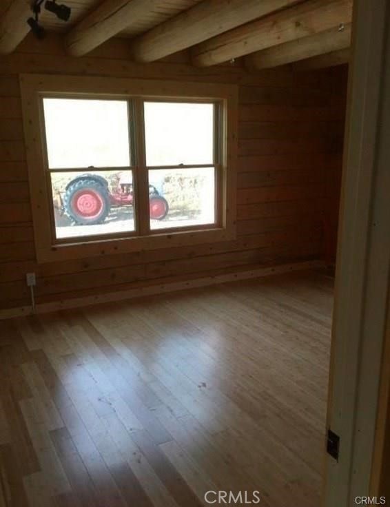 unfurnished room with wood walls, beam ceiling, and hardwood / wood-style floors