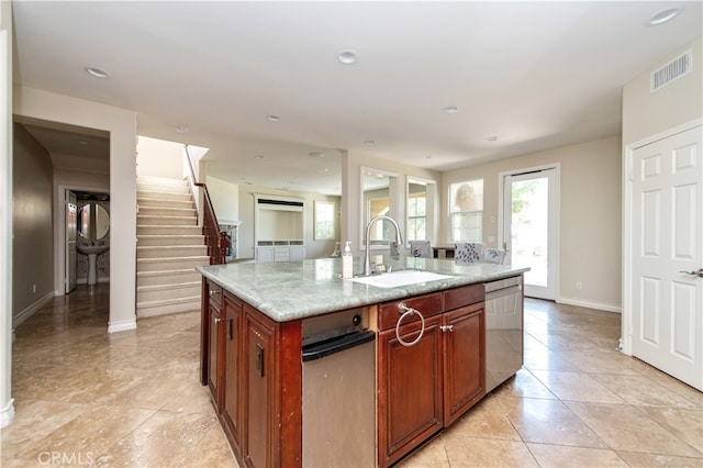 kitchen with light stone countertops, dishwasher, a center island with sink, and sink