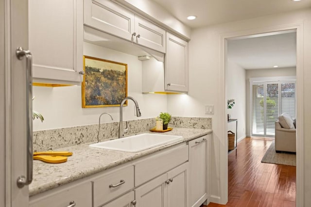 kitchen featuring sink, light stone counters, white cabinets, and dark hardwood / wood-style flooring