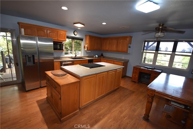 kitchen with light wood-type flooring, black appliances, a center island, ceiling fan, and sink