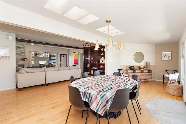 dining area featuring beamed ceiling, light wood-type flooring, and a stone fireplace