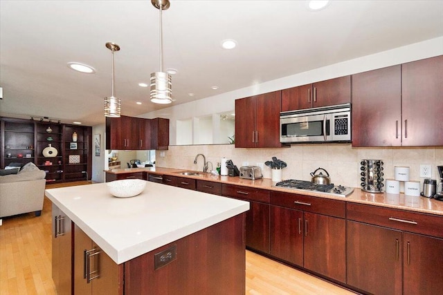 kitchen with pendant lighting, a kitchen island, stainless steel appliances, and light wood-type flooring