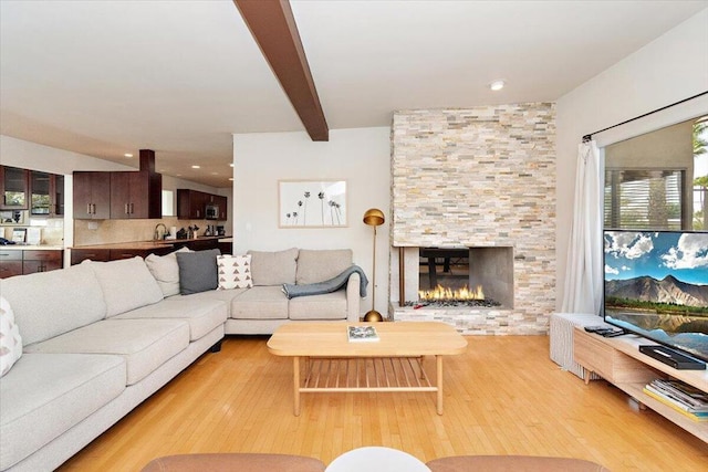 living room with beam ceiling, a fireplace, light hardwood / wood-style floors, and sink