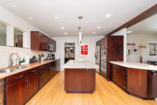 kitchen with appliances with stainless steel finishes, sink, light hardwood / wood-style flooring, a center island, and hanging light fixtures