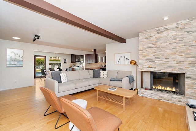 living room with a stone fireplace, beamed ceiling, and light wood-type flooring